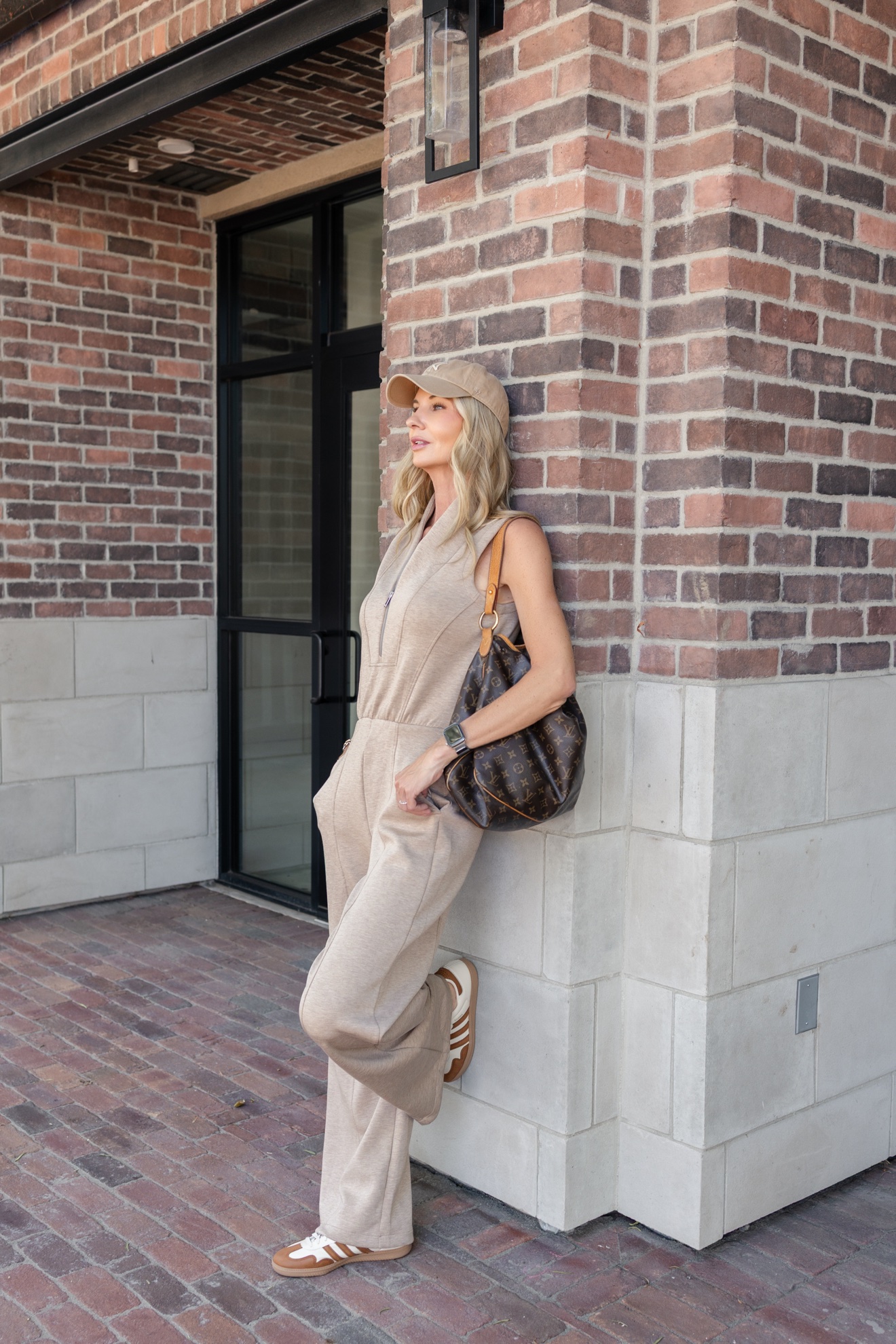 Ris in a beige jumpsuit against a brick wall